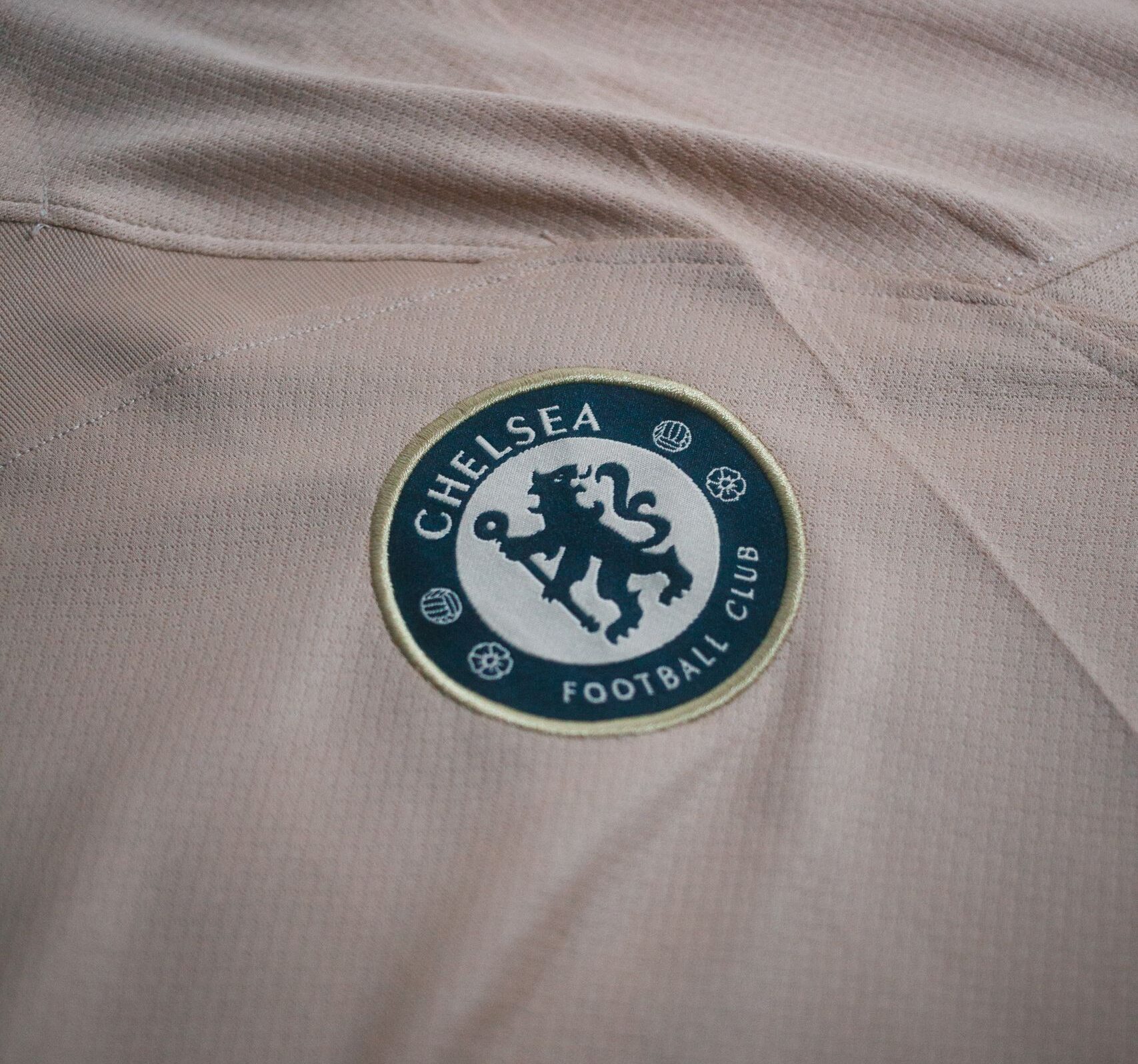 Close-up view of Chelsea Football Club logo on a beige t-shirt, ideal for sports and fashion themes.