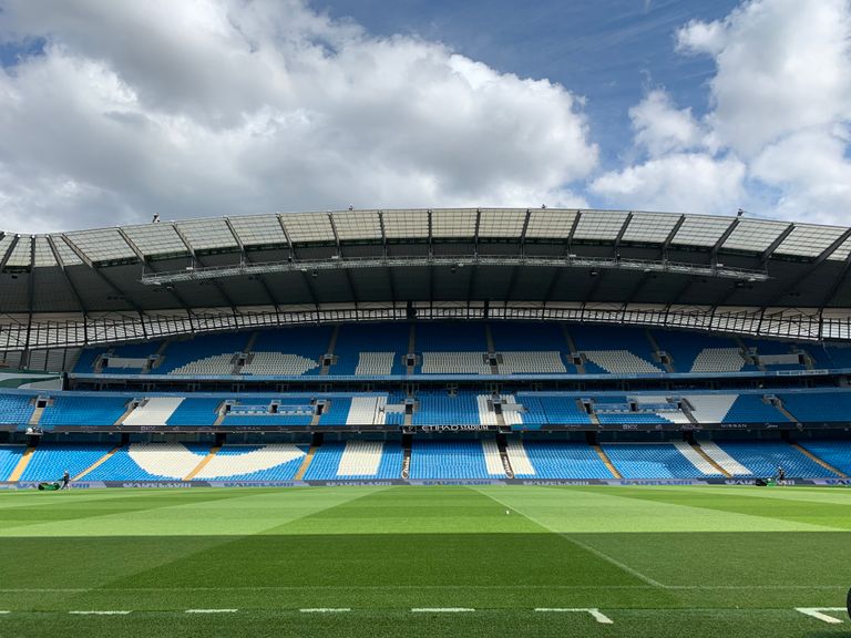 Etihad Stadium in Manchester with empty blue seats under a cloudy sky.